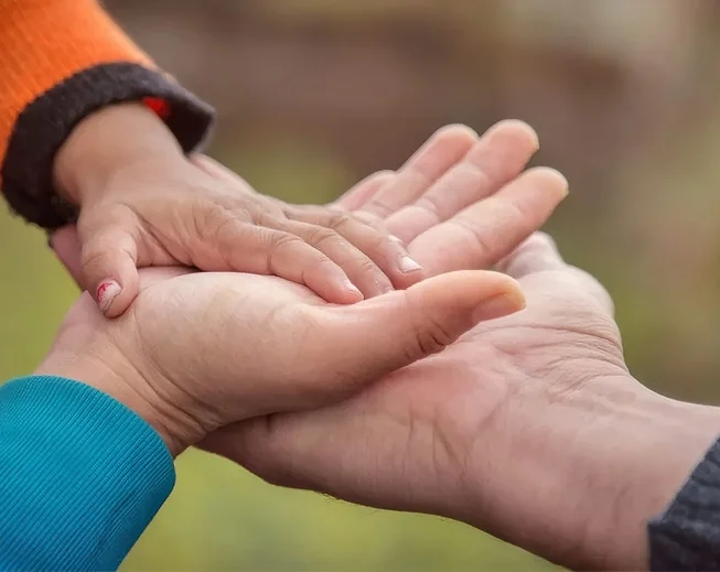 A young child reaching up to hold an adult’s hand
