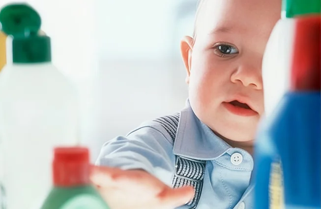 A toddler reaching towards bottles of household chemicals