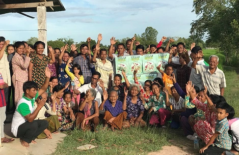 A rural community gathered outdoors, hands raised, holding campaign posters